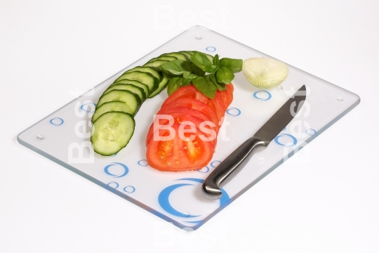 Cucumbers, onions, tomatoes on a glass cutting board