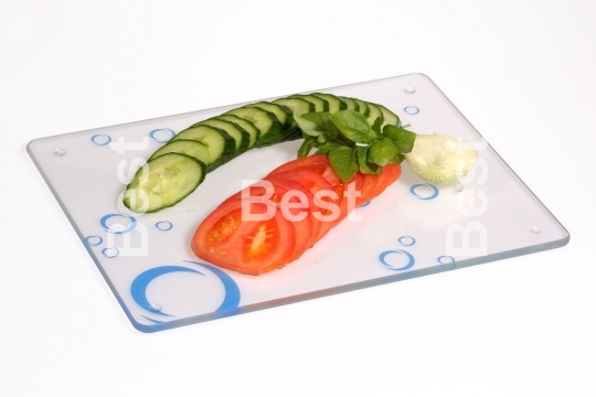 Cucumbers, onions, tomatoes on a glass cutting board